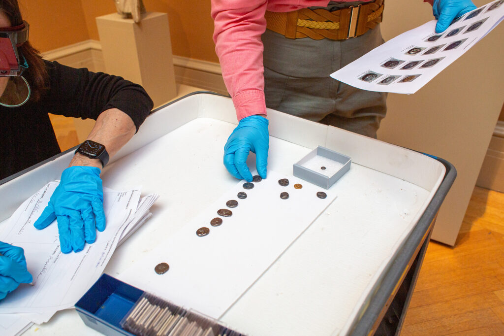 A collections manager checks loaned coins against a paper manifest.