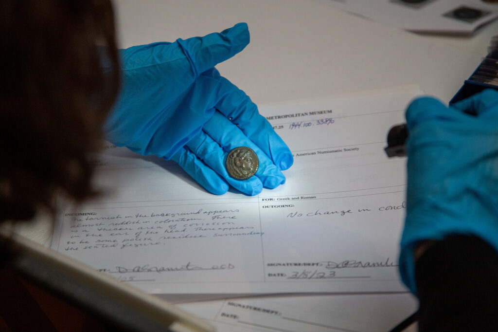 A conservator logs the condition of a loaned coin.