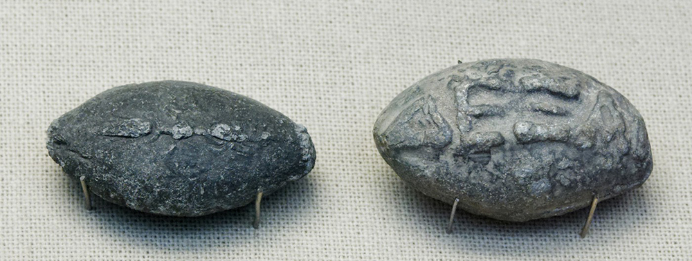 Ancient Greek lead sling bullets engraved with a winged thunderbolt (l.) and “take that!” (r.).